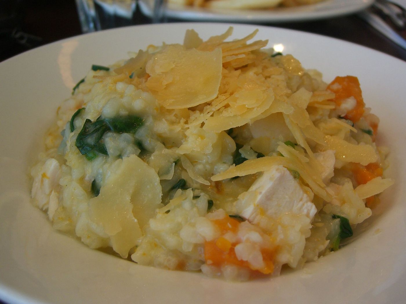 A plate of pumpkin risotto finished with brown butter, crisp sage leaves and grated cheese.